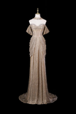 A floor-length champagne beige evening gown with a sequined textured bodice, off-the-shoulder draped sleeves, and a high sheer embellished neckline, displayed on a mannequin against a solid black background.