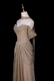 A champagne-colored evening gown with intricate beadwork and sequins, displayed on a white mannequin against a solid black background.