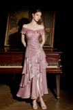 A woman models an off-the-shoulder, metallic dusty pink midi dress with layered ruffles, standing in front of a dark grand piano and a framed painting.