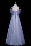 A floor-length off-the-shoulder gown displayed on a mannequin against a black background. The dress has a fitted bodice, a voluminous tulle skirt, and sheer draped sleeves with a matching veil.
