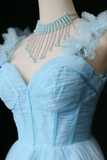 A close-up of a light blue strapless corset dress with ruffled tulle details and a matching pearl choker necklace with silver chains, displayed on a mannequin against a black background.