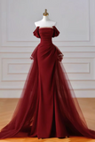 A floor-length off-the-shoulder gown in deep burgundy red, displayed on a white mannequin with a gold neck cap in an indoor studio setting with paneled walls and a wood floor.