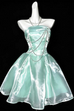 A mint green strapless taffeta dress with a sweetheart neckline, corset-style bodice, and flared skirt, displayed on a white mannequin against a black background. The dress features draped silver chain details on the bodice and waist, and a matching silver necklace is displayed on the mannequin.