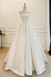 A strapless white ball gown with a structured sweetheart bodice and full skirt, displayed on a mannequin in an indoor room with paneled walls and a patterned rug.