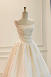 A strapless ball gown dress in a warm ivory or cream satin fabric, displayed on a mannequin with a gold finial against a light cream paneled wall background.