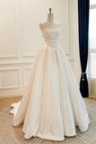 An ivory white satin ball gown displayed on a mannequin in a bright room with white paneled walls and a dark blue velvet curtain.