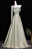 A floor-length formal gown in a pale sage green satin fabric, displayed on a white mannequin against a black background. The dress features an asymmetrical draped neckline with a long matching ribbon detail on one shoulder, a fitted waist, and a full skirt.