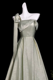 A floor-length off-the-shoulder evening gown in a shimmering pale sage green or light olive metallic fabric, displayed on a white mannequin against a solid black background.