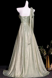 A floor-length formal gown displayed on a white mannequin against a black background. The dress has a shimmering pale sage green color, a one-shoulder design with a draped fabric tie, and a lace-up corset-style bodice.