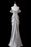 A floor-length off-the-shoulder evening gown in shimmering silver satin, displayed on a white mannequin against a solid black background.