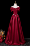 A floor-length off-the-shoulder formal gown in deep burgundy satin, displayed on a cream mannequin against a black background. The dress features a sweetheart neckline, a structured corset-style bodice, a thin silver rhinestone waistband, and a full A-line skirt.