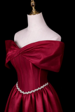 A deep burgundy off-the-shoulder evening gown displayed on a white mannequin torso against a solid black background. The dress features a structured corset bodice, a large bow detail across the shoulders, and a sparkling silver rhinestone belt at the waist.