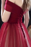 A close-up of a model wearing a deep red off-the-shoulder tulle dress, showing the back of the bodice with a braided lace-up detail.