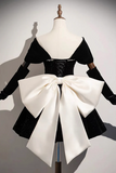 A black velvet costume dress displayed on a mannequin, featuring short puff sleeves, a corset-style bodice with silver rhinestone trim, and a massive oversized white satin bow at the back.
