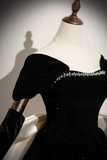 A black velvet off-the-shoulder evening gown with sparkling embellishments and a crystal-embellished neckline, displayed on a white mannequin torso.