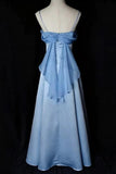 A light blue satin formal gown displayed on a cream mannequin against a black background. The dress features spaghetti straps, a sweetheart neckline, a large bow at the back of the bodice, and a full A-line skirt.