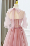 A light pink tulle ball gown displayed on a cream dress form mannequin, viewed from the back. The dress features a sheer tulle high-neck collar with a large bow, a strapless bodice with a sheer back panel, and a voluminous tulle skirt.