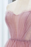 A close-up of a pink tulle dress displayed on a mannequin torso. The dress features a strapless sweetheart neckline, pleated tulle detailing, and a beaded waistband with pink rhinestones.